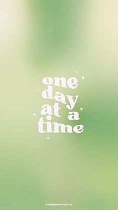 the words one day at a time are written in white on a blurry green background