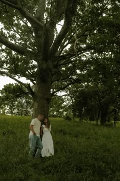 a man and woman standing under a large tree