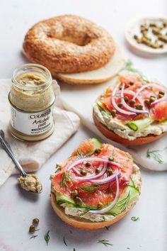 an open face sandwich with onions, tomato and cucumber on it next to a bagel