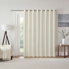 a living room with white curtains and a chair in front of a window that has a painting on the wall