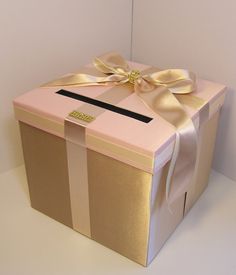 a pink and gold gift box with a bow on the top, sitting on a white surface