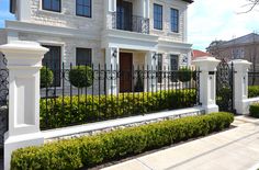 a white house with black iron fence and bushes in the front yard, along side it