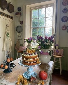 a table topped with a cake next to a vase filled with flowers and fruit on top of it