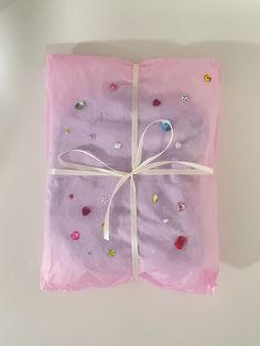 a present wrapped in pink tissue paper with white ribbon and confetti on it