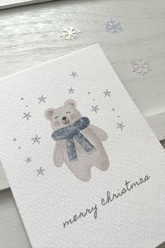 a christmas card with a teddy bear wearing a scarf and snowflakes on it