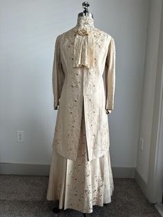 1800s Edwardian Era 3-Piece Daisy Chained Embroidered Light Gold Silk Wedding or Day Suit Dress Measures: Dickie: Neckline:15" Jacket: Bust:  40" Waist:  35" Hip: 42" Shoulder to Shoulder:15" Shoulder to Sleeve Hem:21" Shoulder to Front Hem:40" Shoulder to Back Hem:40" Skirt: Waist:26" Hip: 48" Waist to Hem Front: 38" Waist to Hem Back: 40" Details: -3-Piece Set Includes: Dickie, Jacket and Skirt -Irish Lace, High Collar, Dickie with Front Bow and Tails with Snap Back Closure -Light Gold, Heavy Linen Jacket Bodice with Daisy-Chain, Cotton Embroidery of Light Gold, Gold, and Ecru -Collarless Jacket with Straight Paneled Front with Hook and Eye Closure, Long sSleeves and 3/4 Length Hem -Jacket Embroidered Down Front Closure Panels, Back Yoke, Sleeve Shoulders, Cuffs and Hemline  -Jacket is F Elegant Ceremonial Sets For Transitional Season, Elegant Formal Traditional Wear With Floral Embroidery, Traditional Wedding Dress With Historical Design, Vintage Embroidered Costume Dress, Elegant Ceremonial Raw Silk Set, Formal Gold Raw Silk Dress, Gold Raw Silk Dress For Formal Occasions, Elegant Embroidered Ceremonial Gown, Silk Gown With Intricate Embroidery For Formal Events