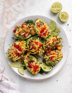 a white plate topped with cucumbers covered in toppings next to sliced limes