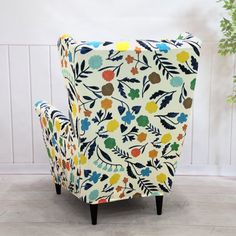 an upholstered chair with colorful flowers and leaves on the back, in front of a white wall