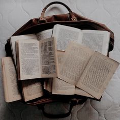 an open book sitting on top of a bed next to a brown bag filled with books