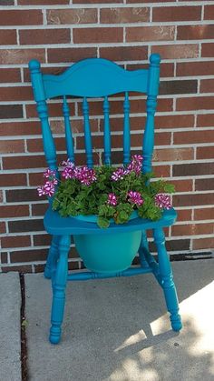 a blue chair with purple flowers in it sitting on the sidewalk next to a brick wall