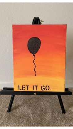 an easel with a painting on it that says let it go and a balloon flying in the sky