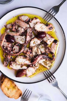 an octopus dish with olives and garlic on a plate next to some silverware