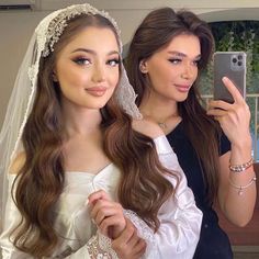 two brides taking a selfie in their wedding day outfits, one wearing a veil and the other holding a cell phone