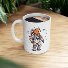 a coffee mug with an astronaut design on the front and side, sitting on a wooden table