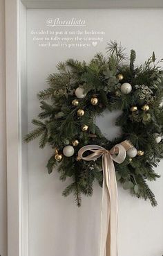 a christmas wreath hanging on the wall next to a white door with a beige ribbon