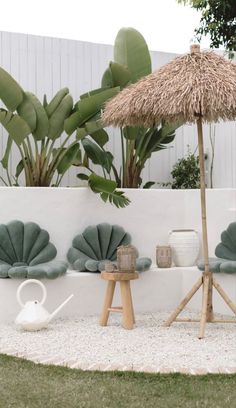 an umbrella and some chairs in a garden with white gravel, grass and palm trees