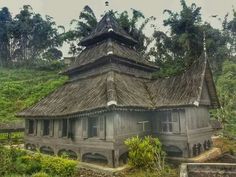 an old building with a thatched roof in the middle of some trees and bushes