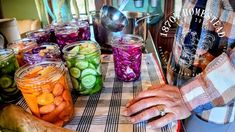 a man standing in front of a table full of jars filled with vegetables and pickles