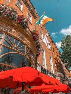 red umbrellas and flowers on the outside of a building with an irish flag flying in the background