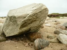 a large rock sitting on top of a sandy beach next to some grass and rocks