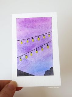 a hand holding up a card with some lights on the wires in front of a purple sky