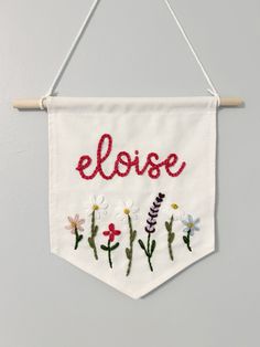 an embroidered banner hanging on a wall with flowers and the word eloee written in red