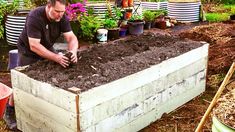 a man kneeling down in front of a garden box filled with dirt