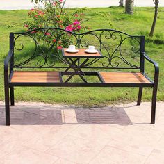 a bench with two cups on it sitting in front of a flower pot and table