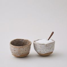 two ceramic bowls with spoons in them on a white surface, one has brown speckles