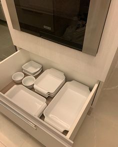 an open drawer in a kitchen with dishes and trays on the bottom, next to a microwave