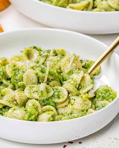 a white bowl filled with pasta and broccoli covered in pesto cheese sauce