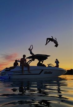 two people are jumping off the back of a boat into the water at sunset while another person is diving