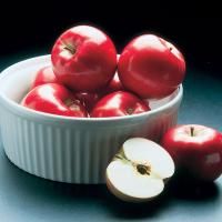 apples in a white bowl with one cut open and the other half sliced up, on a blue surface