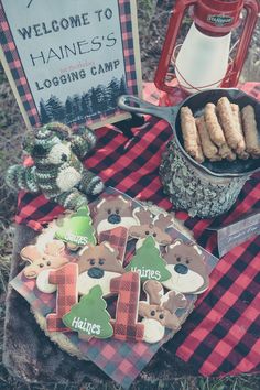 there is a picnic table with cookies and other items on the blanket, including a sign that says welcome to maine's logging camp