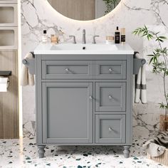 a bathroom vanity with marble counter top and grey cabinet, under a round mirror on the wall