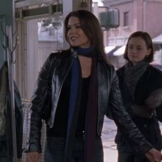 two women are walking down the street in front of a store window and one is wearing a black leather jacket