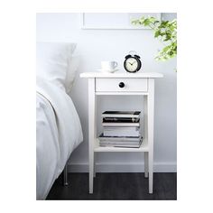 a nightstand with books and a clock on it next to a white bed in a bedroom