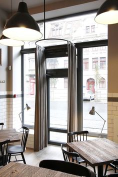 an empty restaurant with wooden tables and chairs in front of large windows that look out onto the street