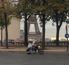 a person riding a motorcycle down the street in front of the eiffel tower