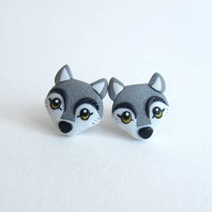 two small gray and white raccoon earrings on a white surface with yellow eyes