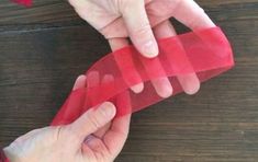 two hands holding red tape on top of a wooden table next to another person's hand