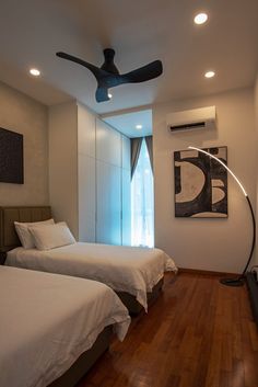 two beds in a room with wooden floors and ceiling fan above them, along with pictures on the wall