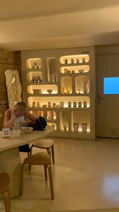 a woman sitting at a table in front of a wall full of shelves with candles