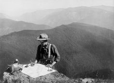 a man standing at the top of a mountain writing on a map while holding a camera