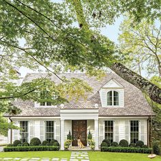 a white house with lots of trees and grass on the front lawn, surrounded by hedges