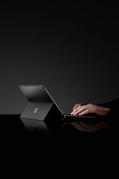 a person using a laptop computer on a black table in the dark with their hand resting on the keyboard