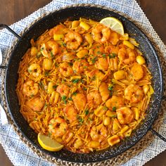 a skillet filled with shrimp and pasta on top of a table next to lemon wedges