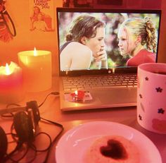 a laptop computer sitting on top of a desk next to a pink plate and cup