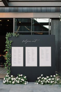 the seating plan for this wedding is displayed on a large black board with white flowers and greenery