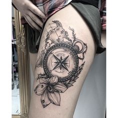 a woman's thigh with a compass and flowers tattoo on the side of her leg